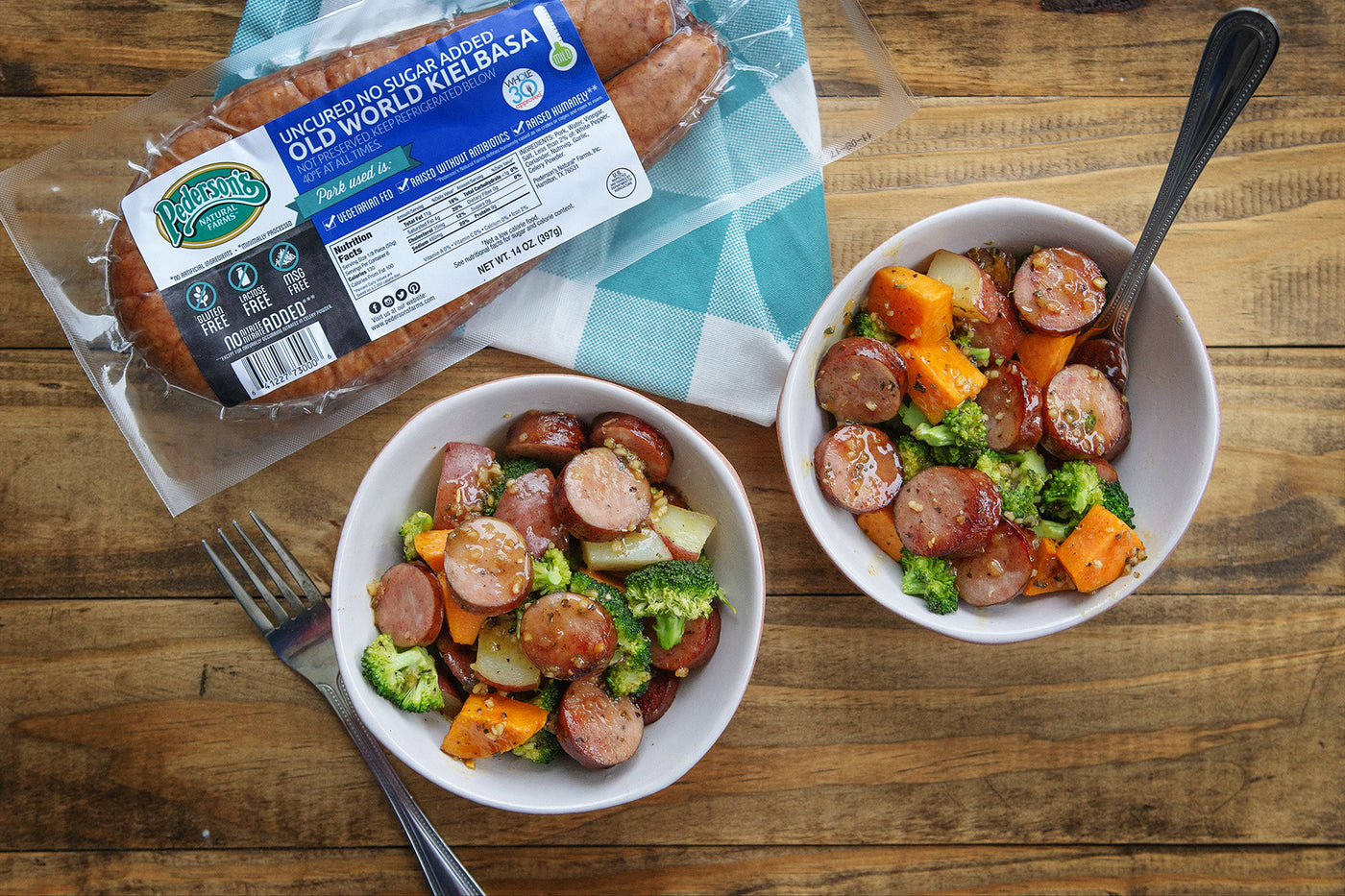 Two bowls of stir fry with gluten free keilbasa sit on a wooden table with a package of Pederson's Farms no sugar gluten free keilbasa next to it.