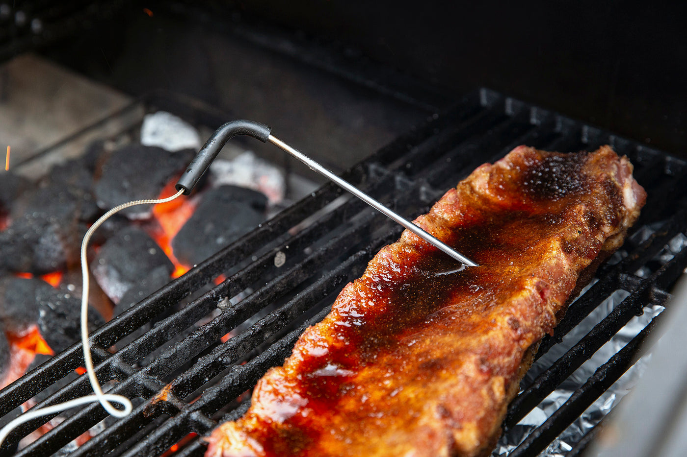 A rack of ribs are shown on the grill with a thermometer stuck in the meat.