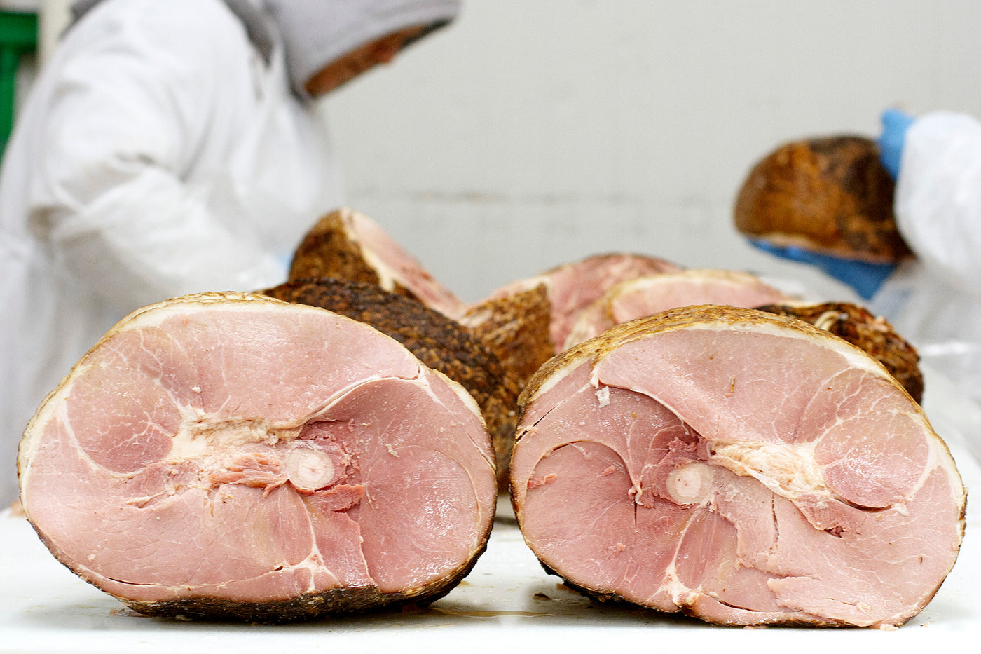 Two bone in hams sit on a counter in the Pederson's Farms plant. Workers are seen in the background preparing the hams.