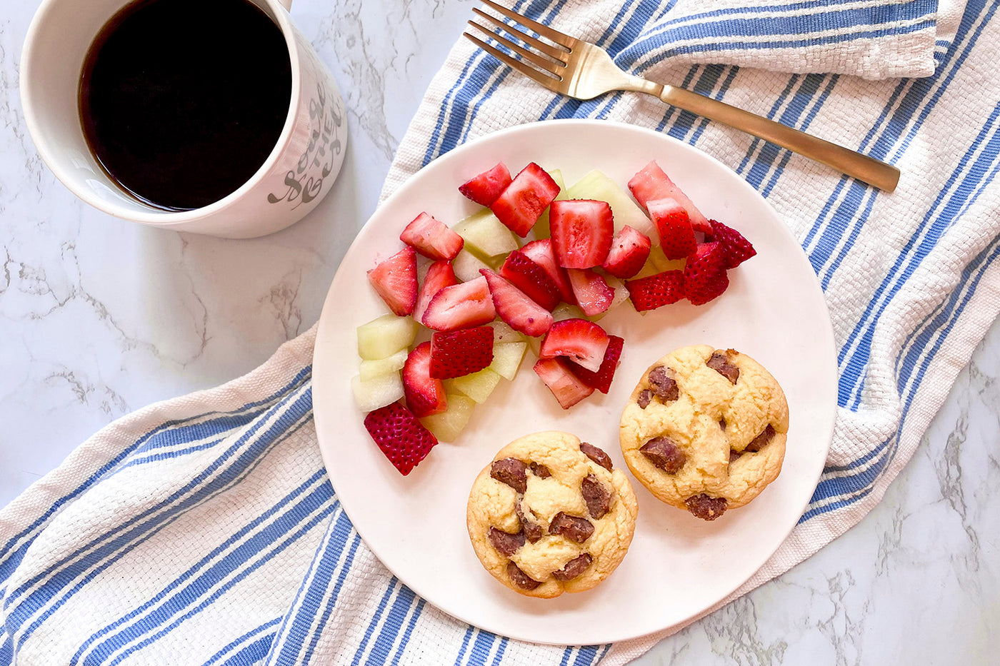 Sausage Pancake Muffins sit one a white plate with strawberries and coffee on the side.
