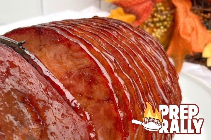 Close up of a sliced Brown Sugar & Bourbon Glazed Ham sitting on a white platter with fall decorations in the background.