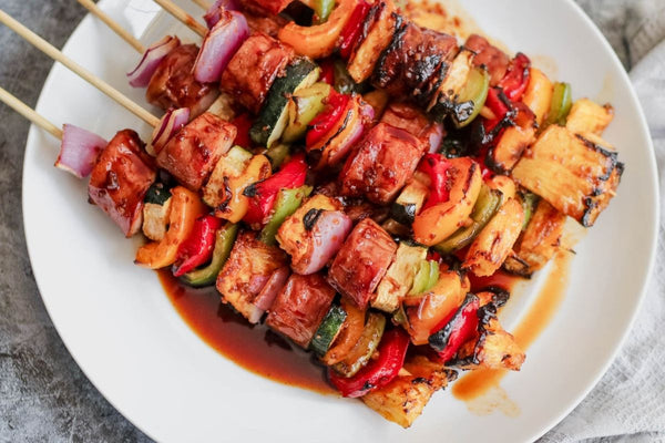 Grilled kielbasa kebabs with colorful bell peppers, pineapple, and red onion on a white plate, brushed with a glossy coconut aminos glaze.
