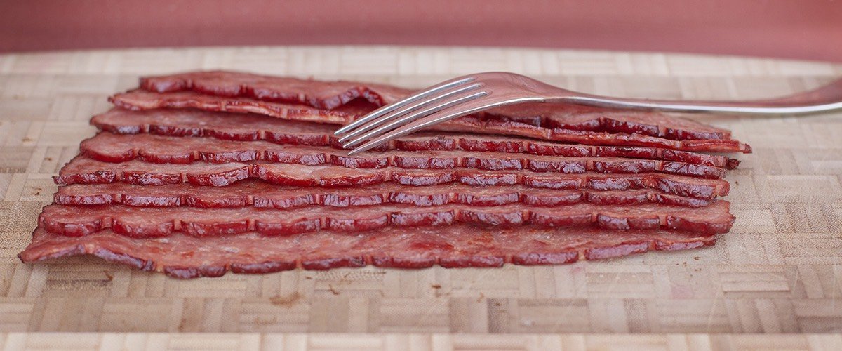Oven baked turkey bacon laying on a cutting board with a fork.