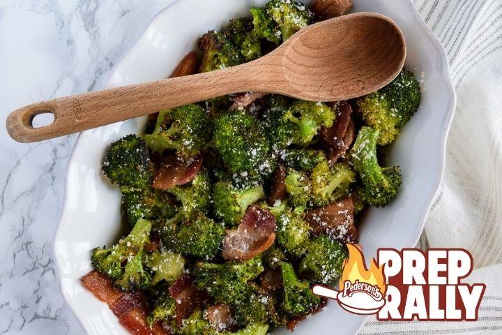 Parmesan Roasted Broccoli with Bacon sits in a white serving bowl with a wooden spoon rested on top of it.