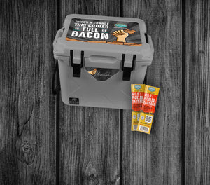 A custom gray Bison cooler is shown against a weathered wood background. The cooler has a top that says "There's a chance this cooler is full of bacon" with the Pederson's Farms logo. There are also two packages of mild pickled sausage in the corner.
