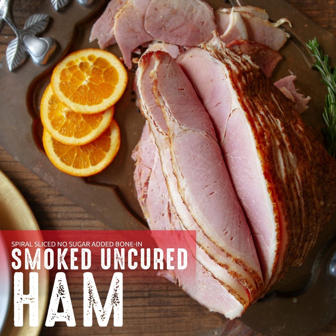 Spiral Sliced No Sugar Added Bone-In Smoked Uncured Ham lifestyle image with label overlay. The ham is positioned on a tray with orange slices and green garnish