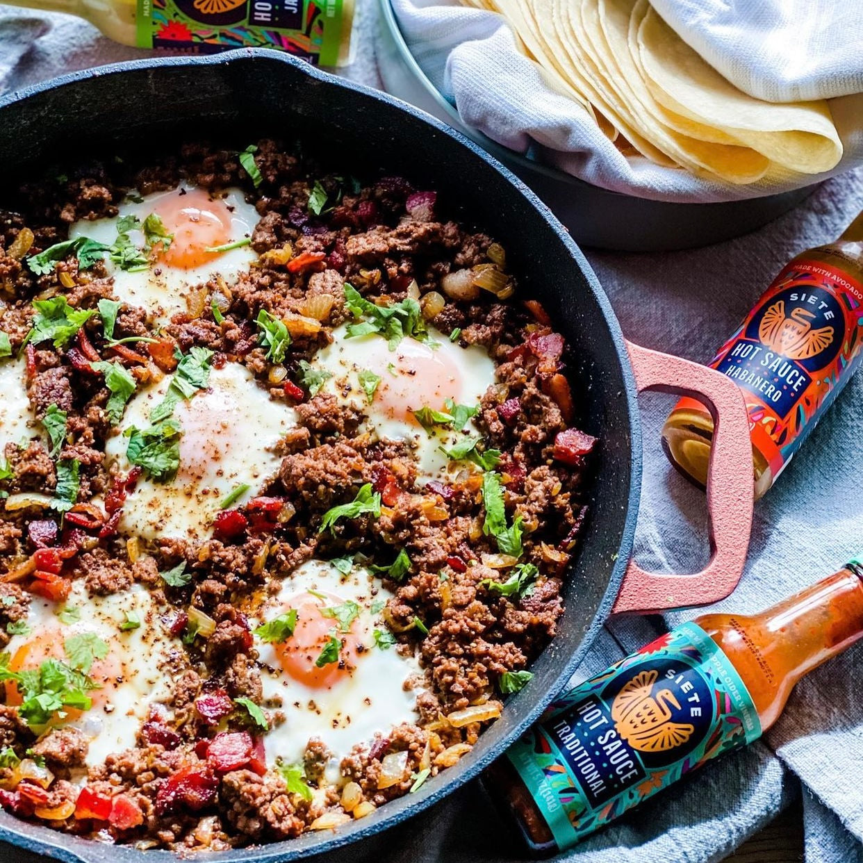 Taco dish with Chorizo and several sunny-side-up eggs topped with cilantro, served with Siete hot sauce.