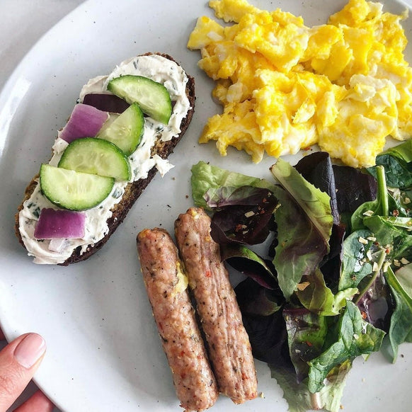 Breakfast served with two fullly cooked mild breakfast sausage links, a small salad, scrambled eggs and a peice of bread topped with large slices of onion and cucumber over a cream spread.