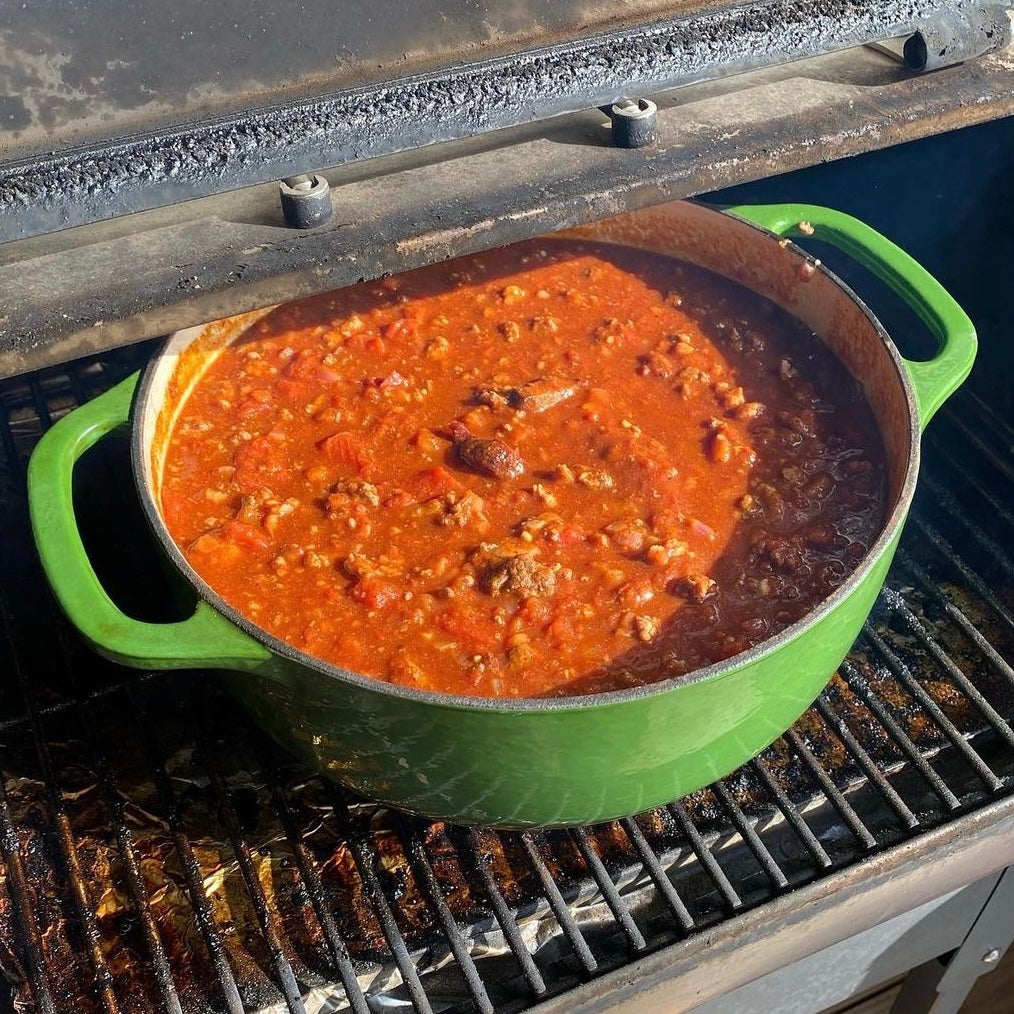 Large green pot of Chili on the grill outside.
