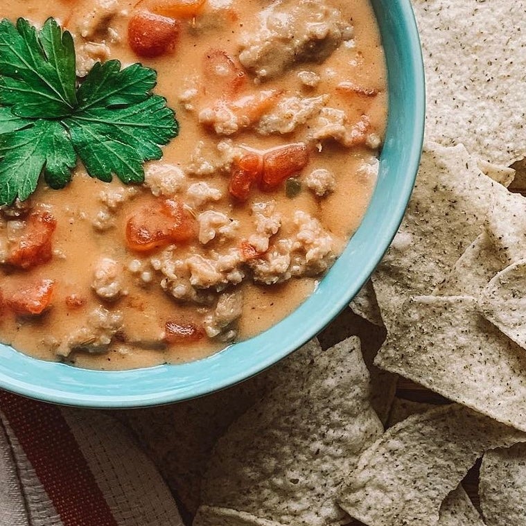 Creamy bowl of tomato and Ground Beef soup with triangle corn chips surrounding the bowl.