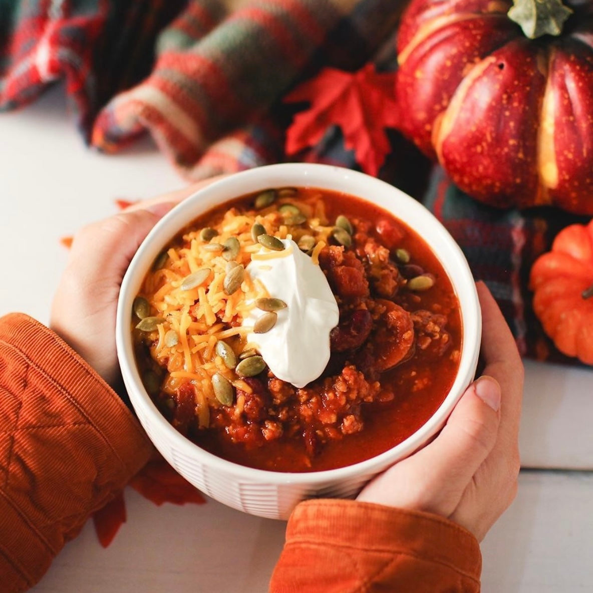 Hands holding a bowl of Pedersons Ground Beef chili to warm up.